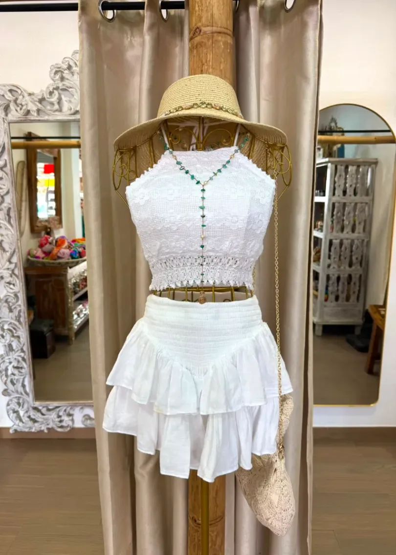 Top blanco sin mangas y falda de capas en un maniquí con sombrero de paja en el escaparate de una boutique.