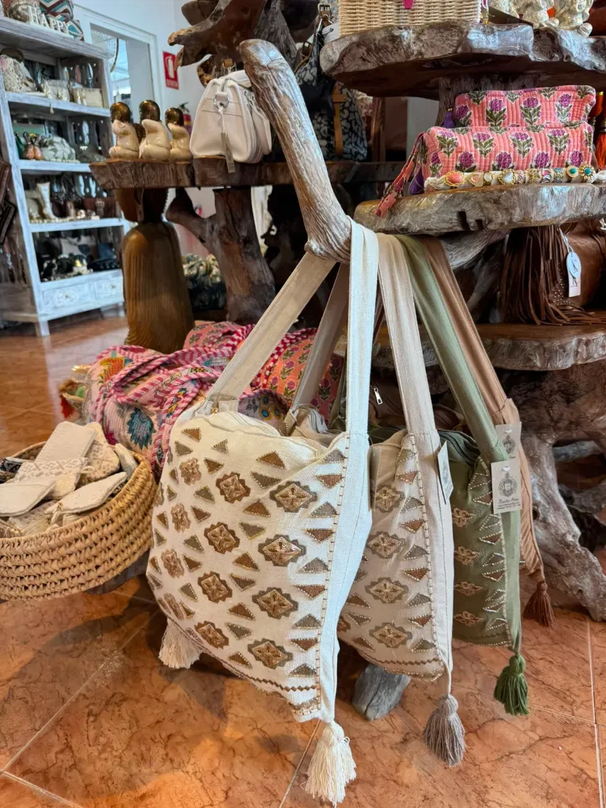 Bolsos de tela tejidos con borlas expuestos en una boutique junto a coloridos cojines y cestas.
