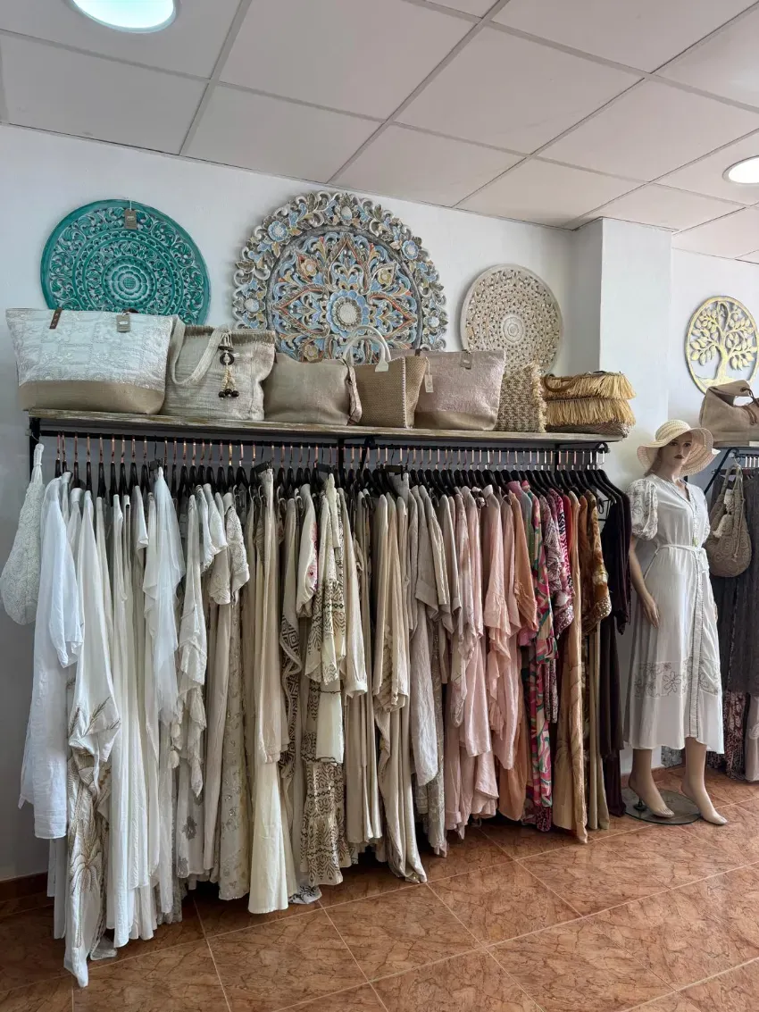 Perchero de boutique con vestidos y bolsos en tonos neutros, además de obras de arte decorativas para la pared y un maniquí.