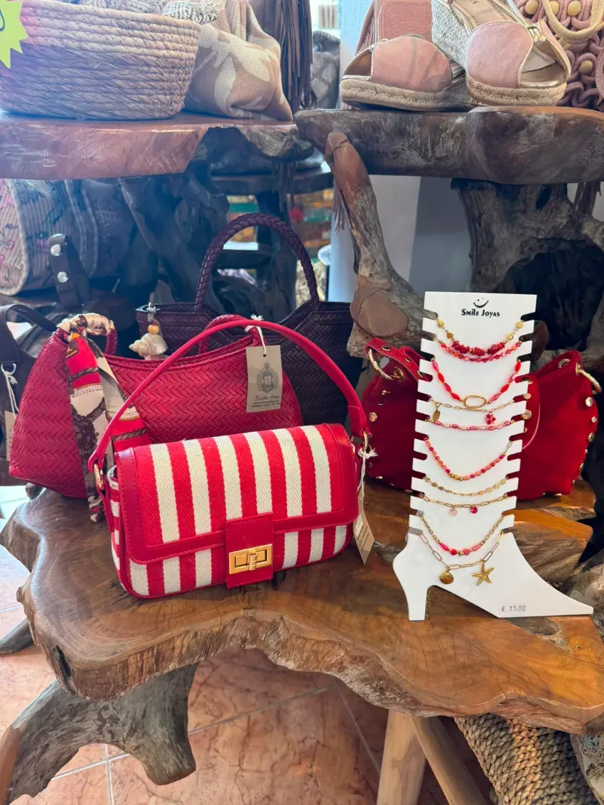 Un bolso de rayas rojas y blancas junto a un collar de cuentas blancas se exhiben en un estante rústico de madera.