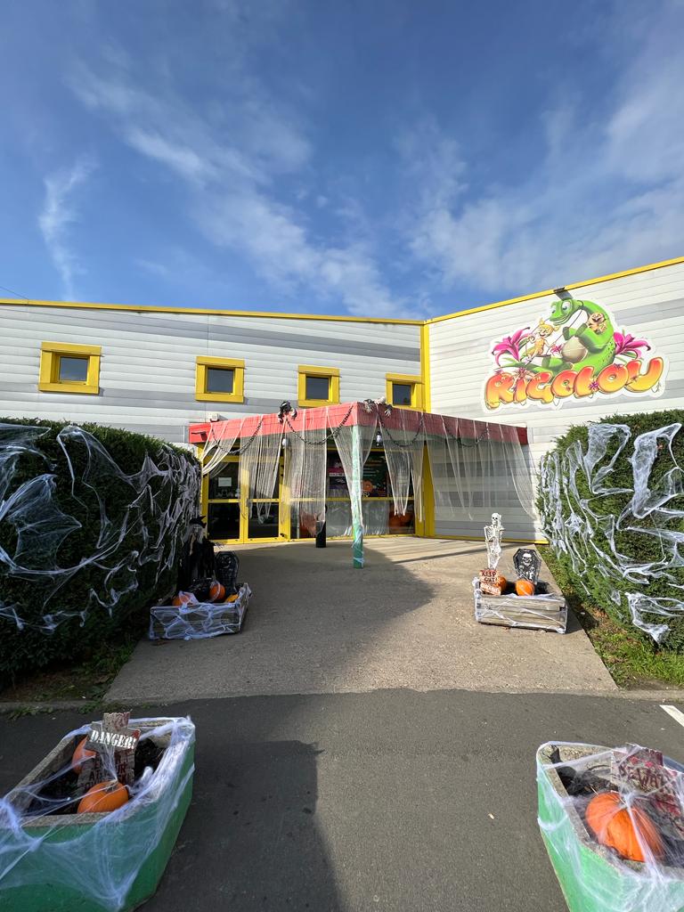 Devanture du Rigolou décoré pour Halloween ; décorations vertes, jaunes et oranges avec des toiles d'araignée et des cercueils.