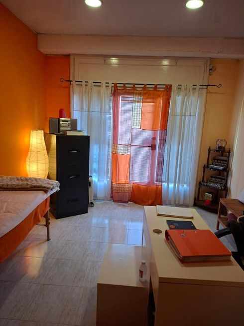 Interior de sala de masajes con pared naranja, mesa de masajes y archivador. Puerta con cortinas.