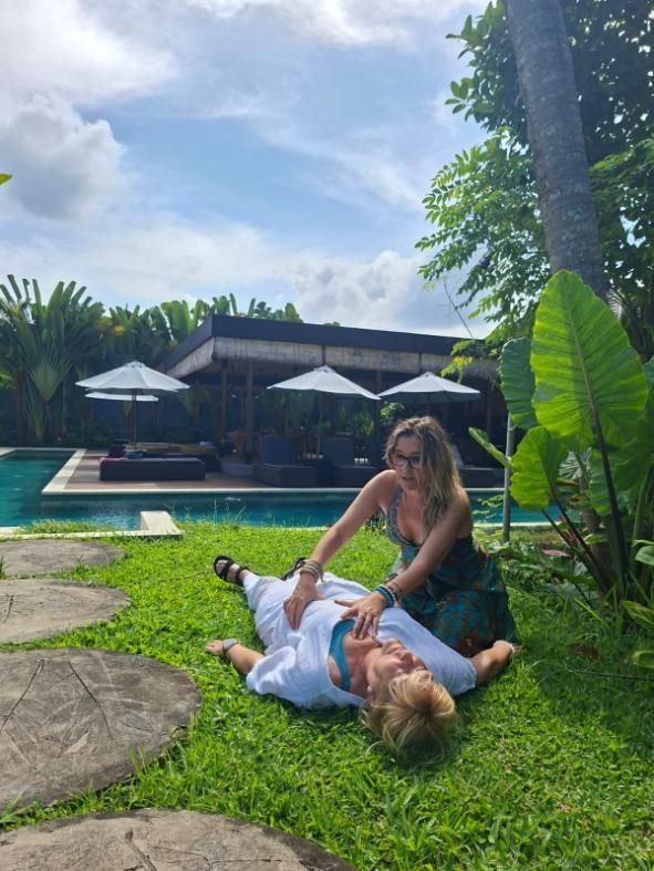 Mujer administrando compresiones torácicas al aire libre cerca de una piscina. Día soleado, césped verde, ambiente informal.