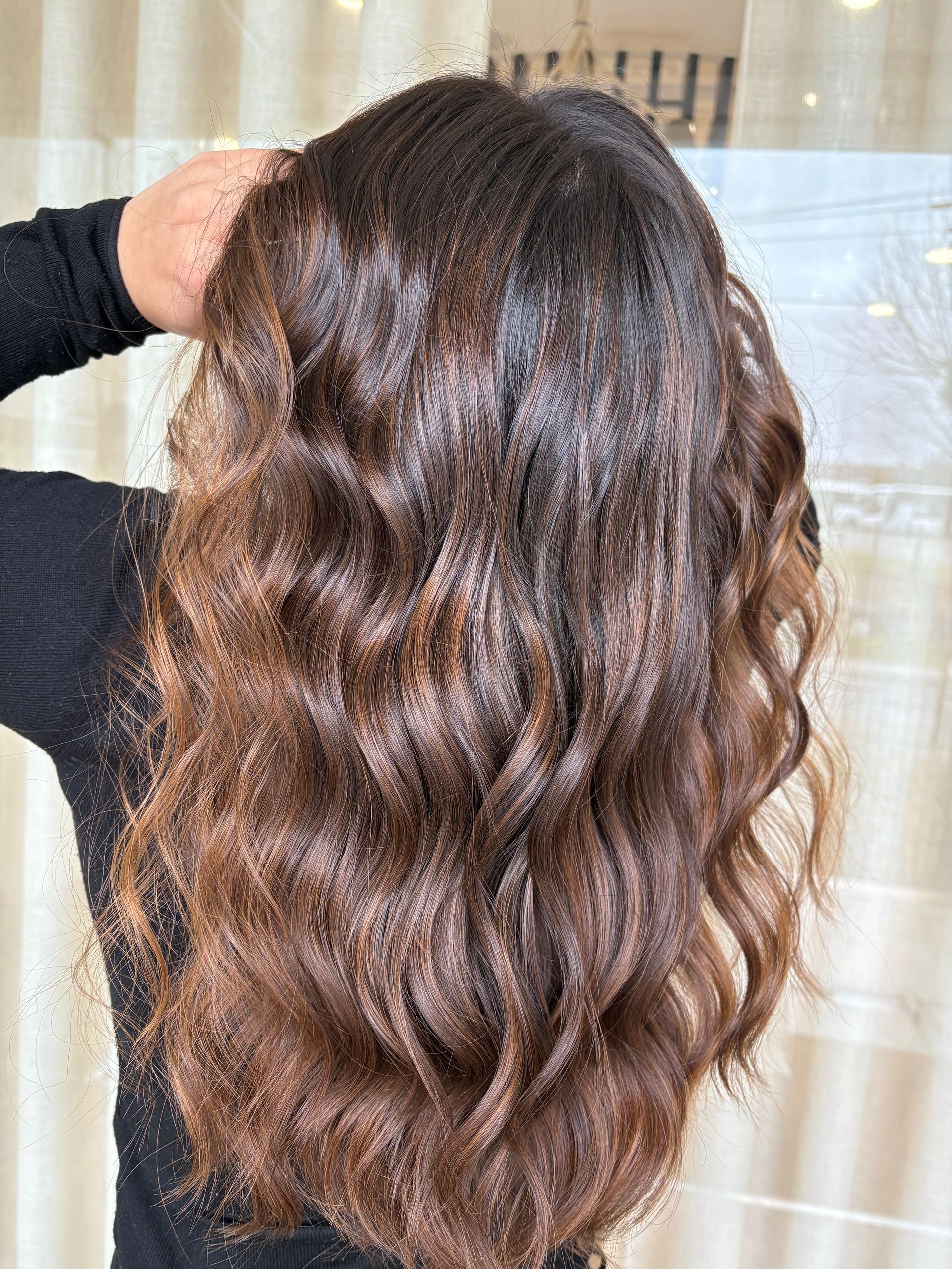 Cabelo castanho comprido e ondulado, escuro na raiz e clareando nas pontas.