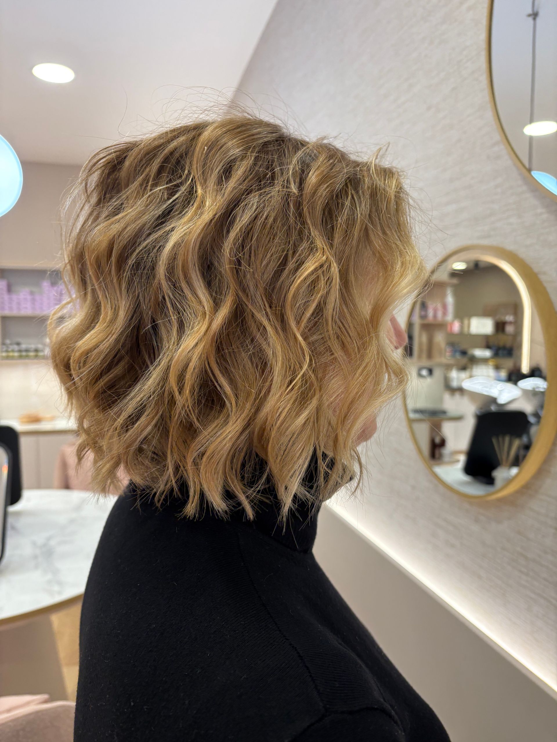 Mulher com cabelo castanho claro ondulado e em camadas, sentada em um salão de beleza.