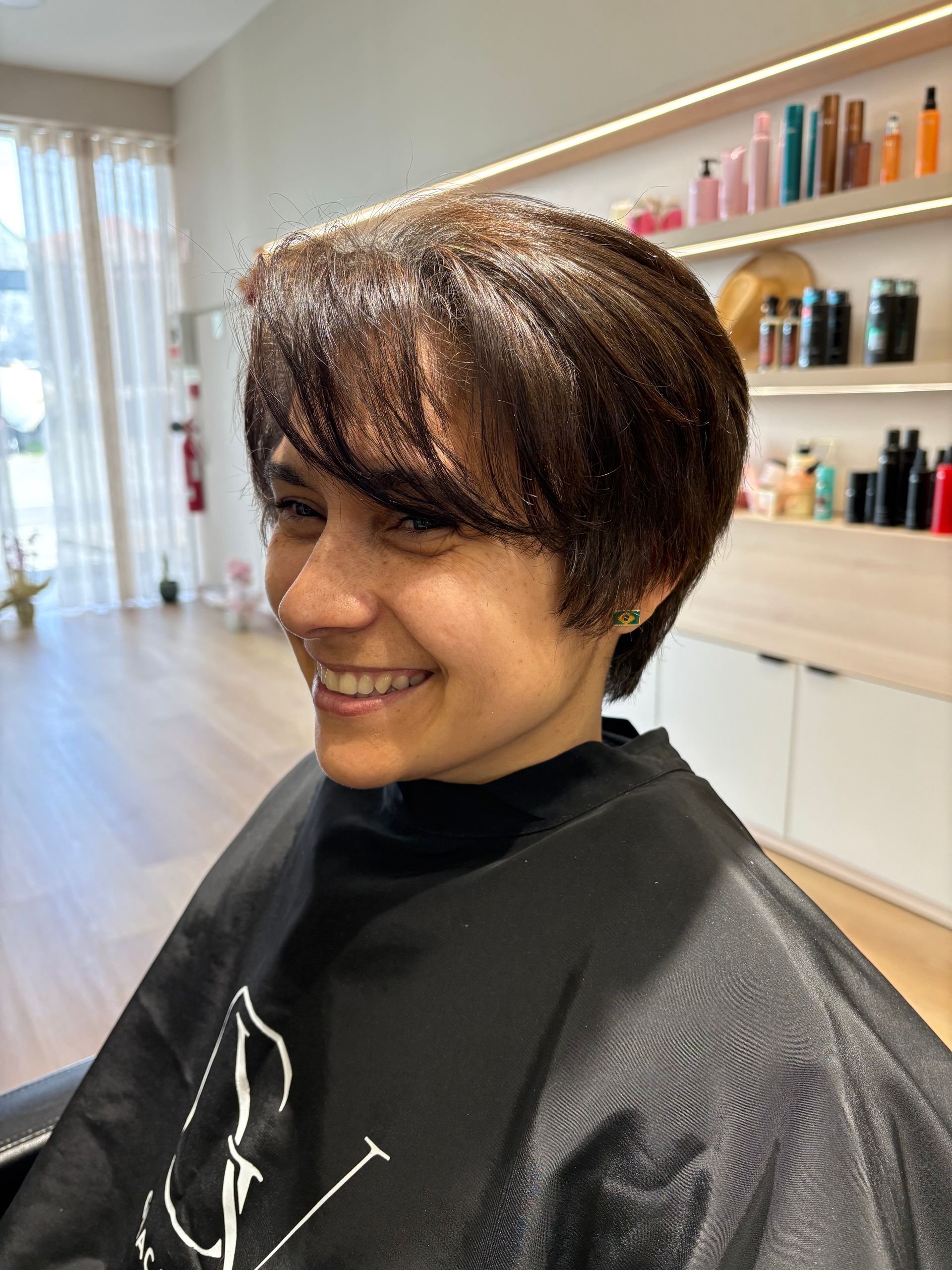 Mulher com cabelos ondulados castanho-escuros. Ela está vestindo uma blusa branca.