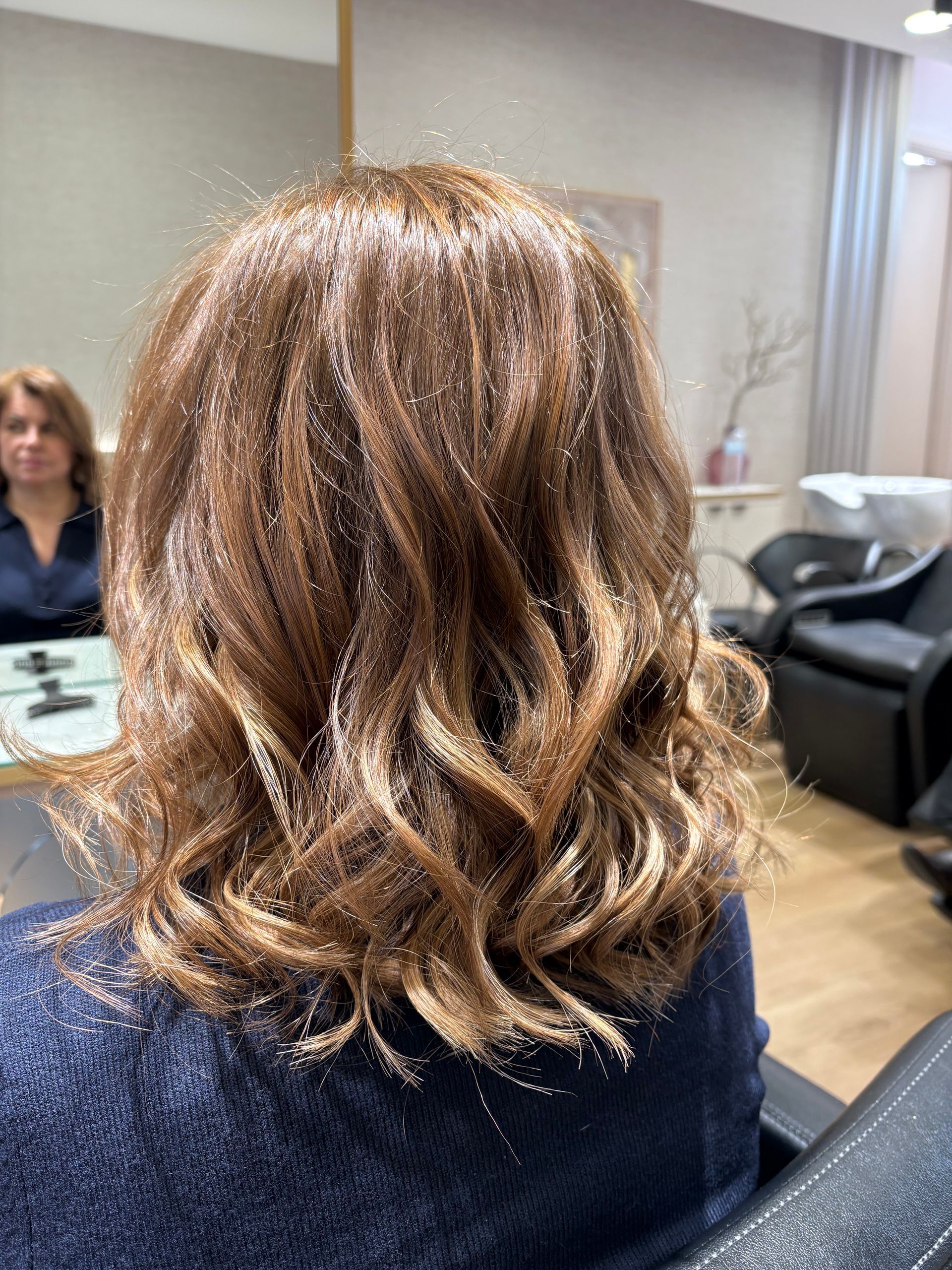 Mulher com cabelo castanho ondulado, com mechas em tons mais claros, contra um fundo branco.