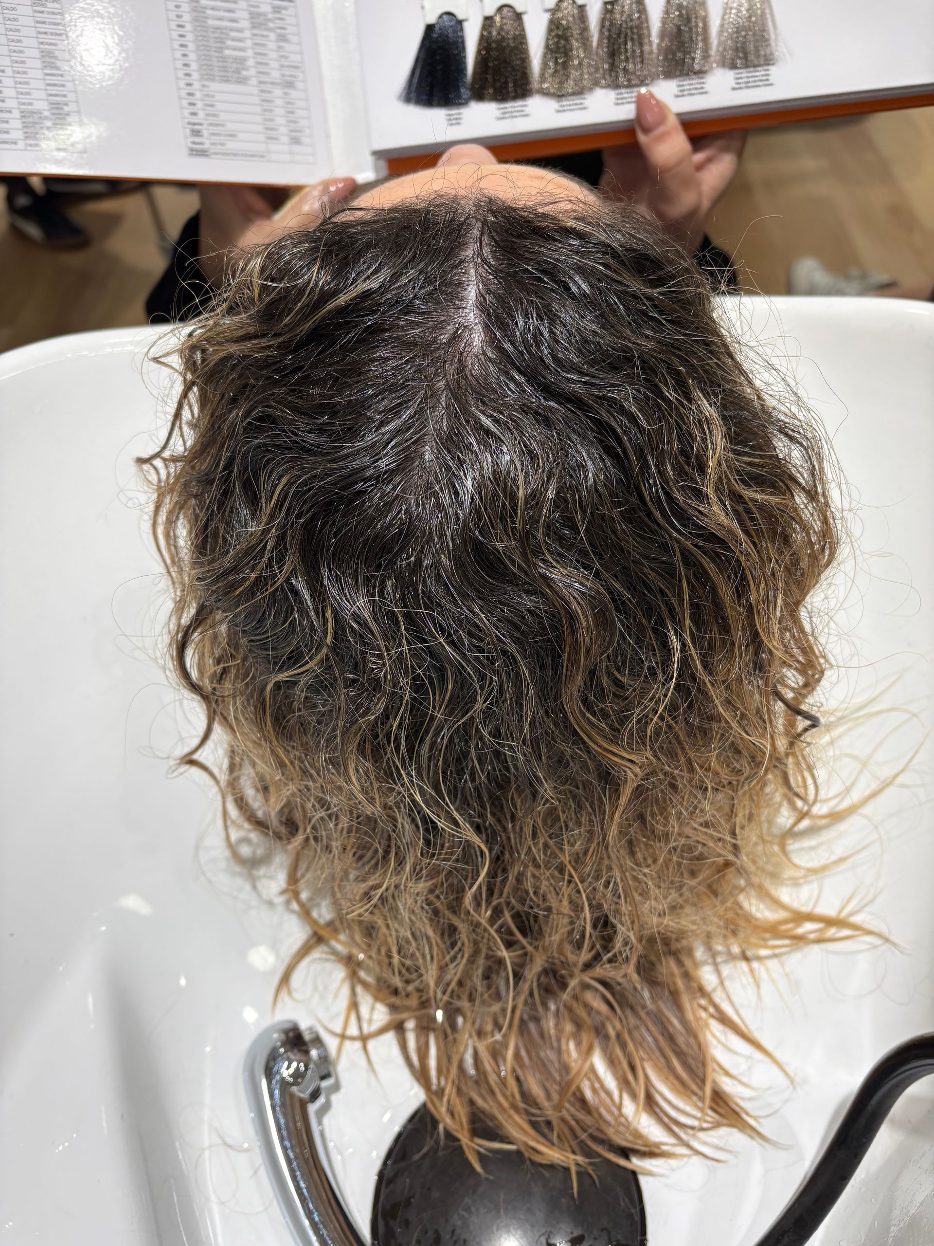 Mulher com longos cabelos castanhos ondulados em frente a uma prateleira de produtos de beleza.