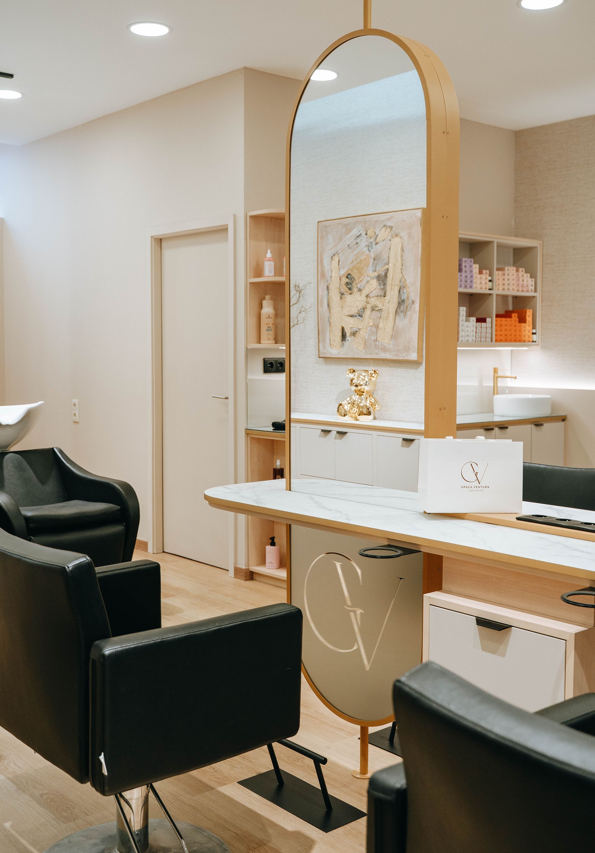 Interior de salão de cabeleireiro com estações de trabalho, cadeiras, espelho e obras de arte decorativas.