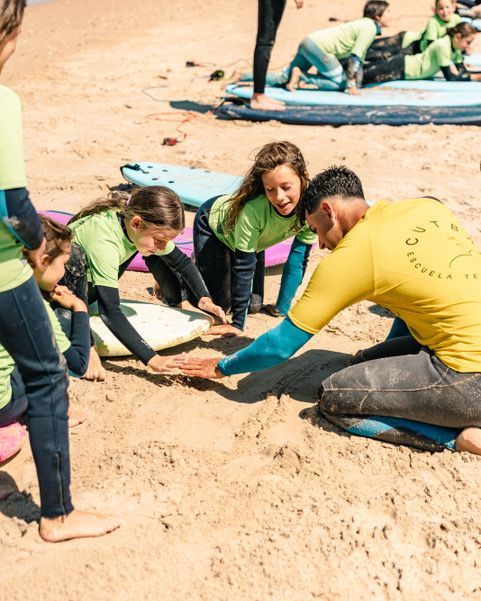 Un grupo de niños están de pie sobre tablas de surf en una playa.