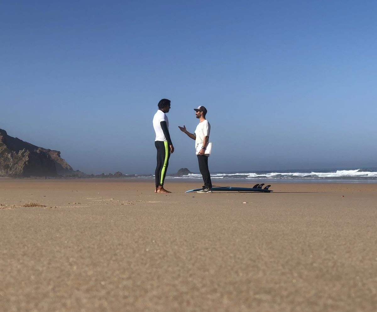 Dos hombres están parados en una playa hablando entre sí.