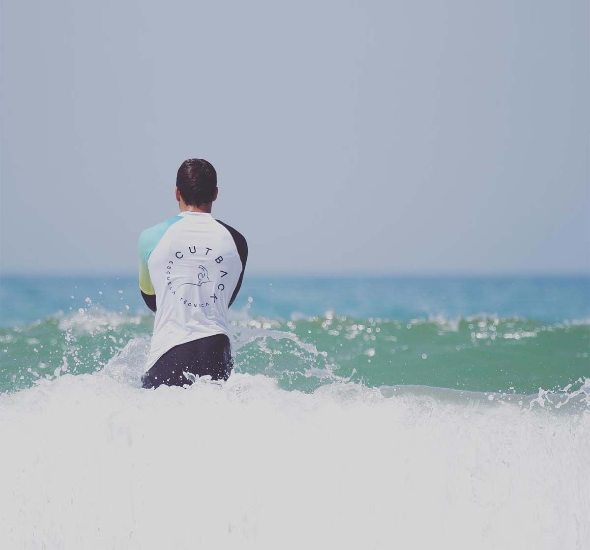 Un hombre está sentado en una tabla de surf en el océano mirando las olas.
