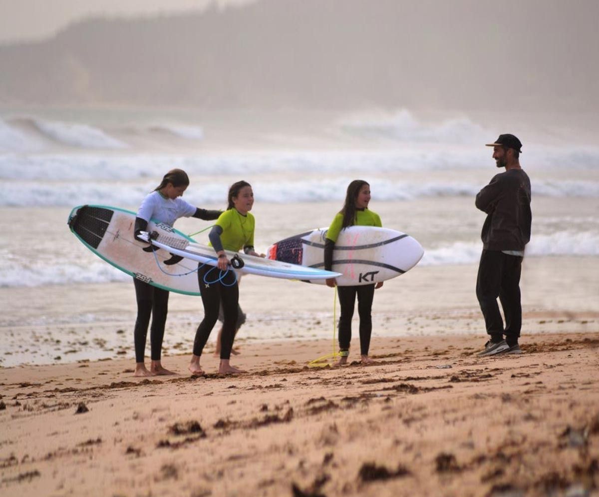 Un grupo de personas llevando tablas de surf en una playa.