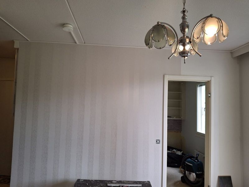 Tyhjä huone, jossa on raidallinen tapetti, kattokruunu ja avoin oviaukko pieneen viereiseen huoneeseen.