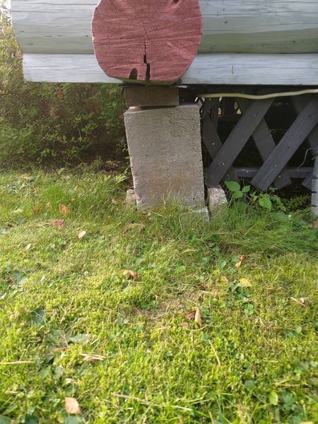Valkoinen talon ulkoverhous, jossa on vaaleanpunainen pyöreä merkki betonilohkossa nurmikkoisen pihan yläpuolella.