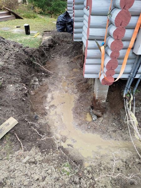 Mutainen kaivanto hirsimökin seinän vieressä, jossa on lammikoita kaivannossa.