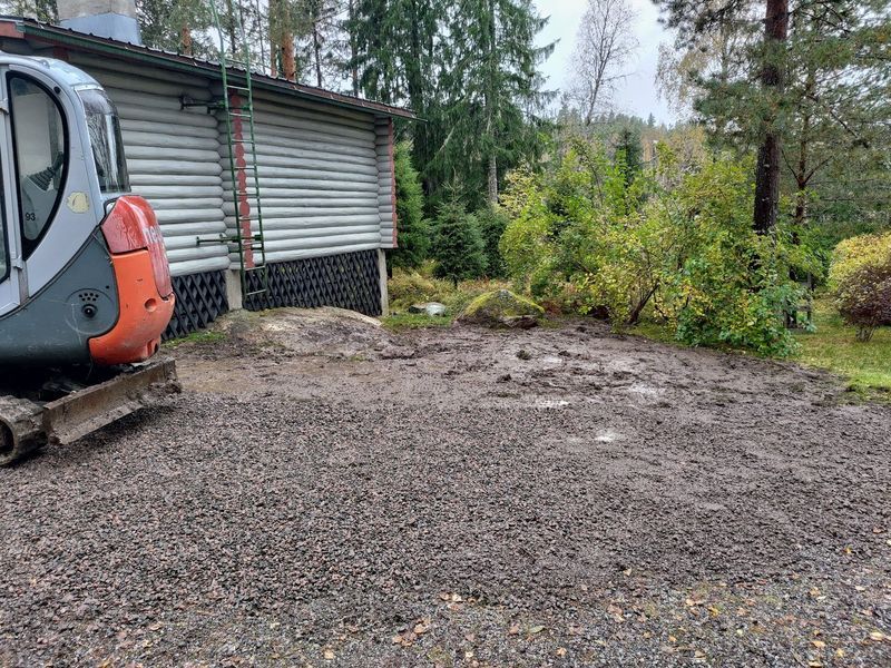 Oranssinharmaa kaivinkone sorapalstan ja metallivajan vieressä metsäalueella