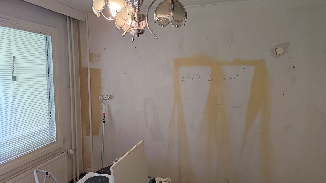 Pieni huone, jossa on valkoiset seinät, ikkuna, kattokruunu ja keltaisia ​​maalilaikkuja seinillä.