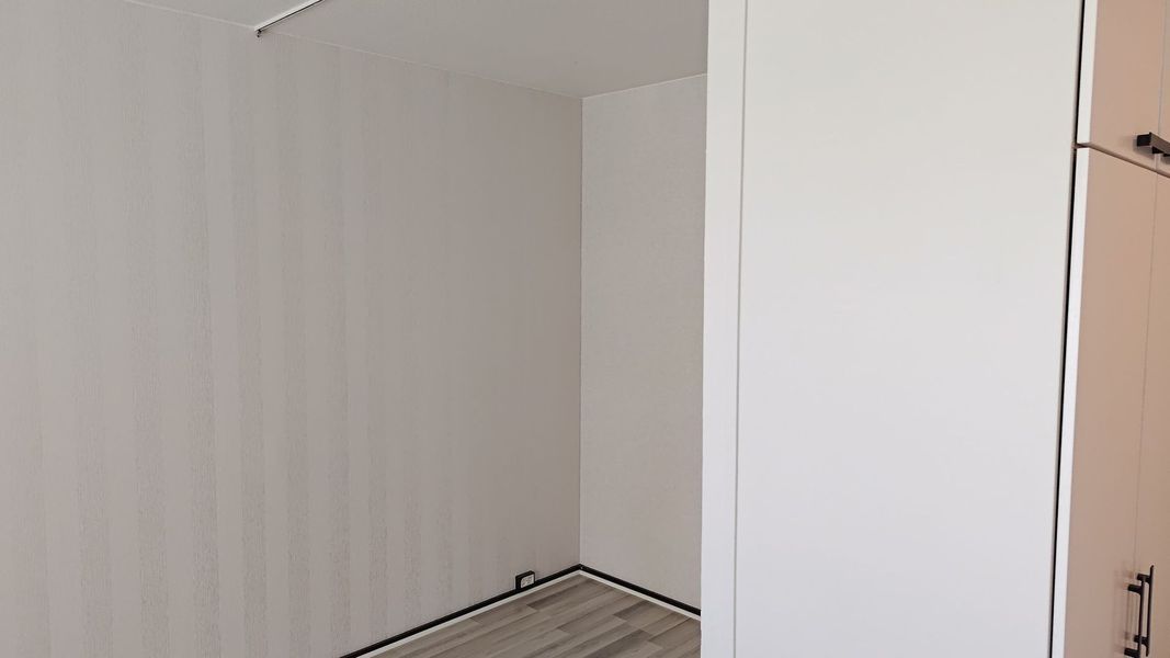 Tyhjä valkoinen vaatekaappi liukuovilla ja beigenvärisillä seinillä pienessä huoneessa.