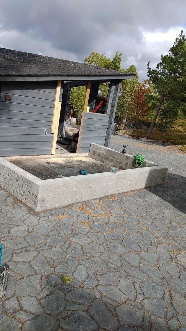 Kivinen patio, jossa suorakaiteen muotoinen korotettu istutuslaatikko harmaan talon ja katon räystään vieressä.