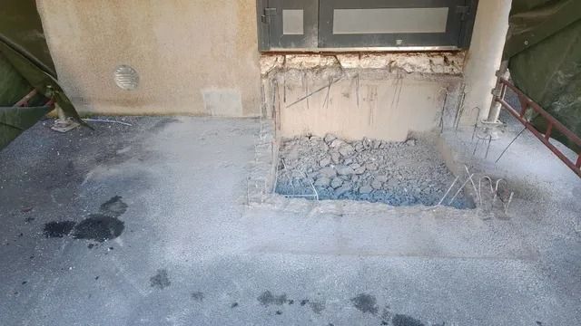Betoninen terassi, jossa on tummia tahroja ja vaurioitunut seinän pohja ikkunan alla.