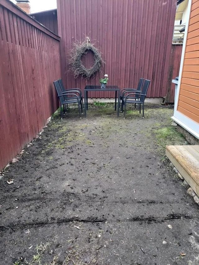 Pieni takapihan patio, jossa on kolme mustaa tuolia, pöytä ja seppele punaisella puuaidalla.