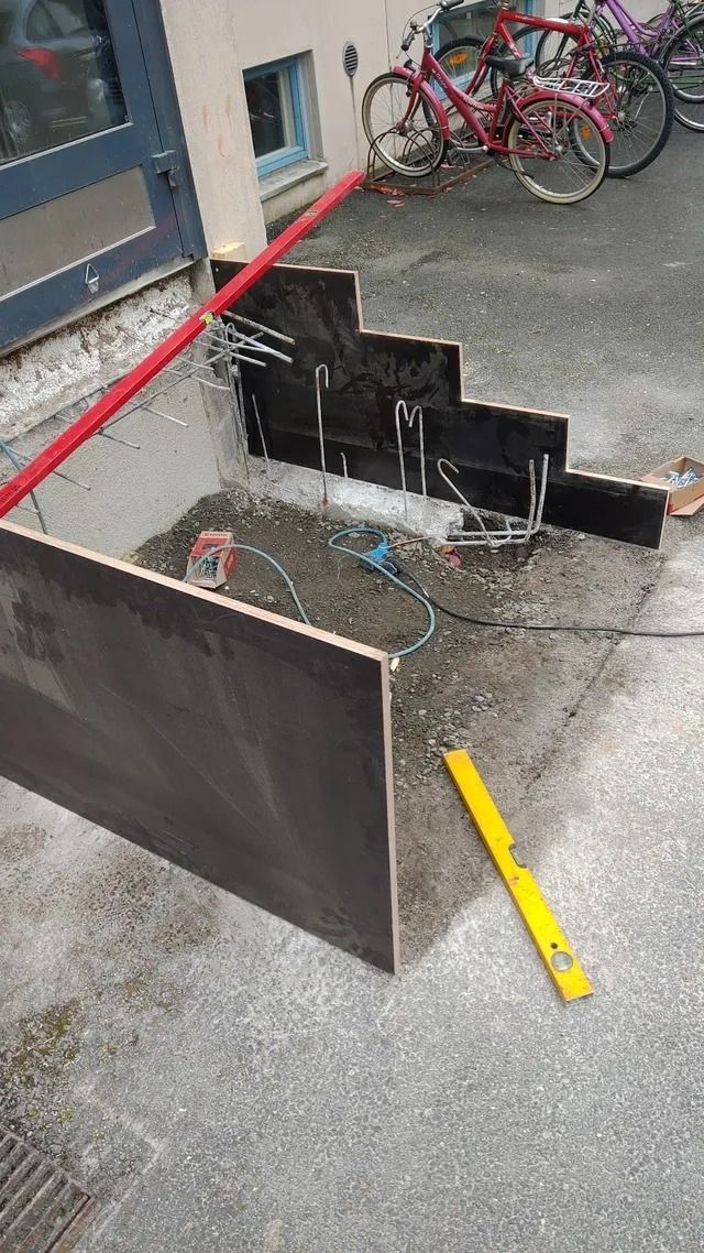 Rikkoutunut musta kyltti ja roskia jalkakäytävällä byrokratian vieressä, taustalla polkupyörät.
