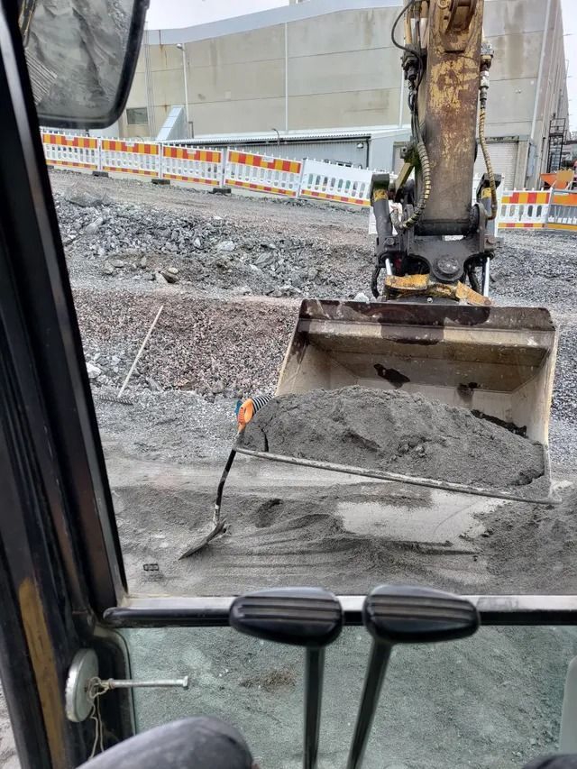 Kaivinkoneen kauha kauhaa soraa rakennustyömaalla lasi-ikkunan takana