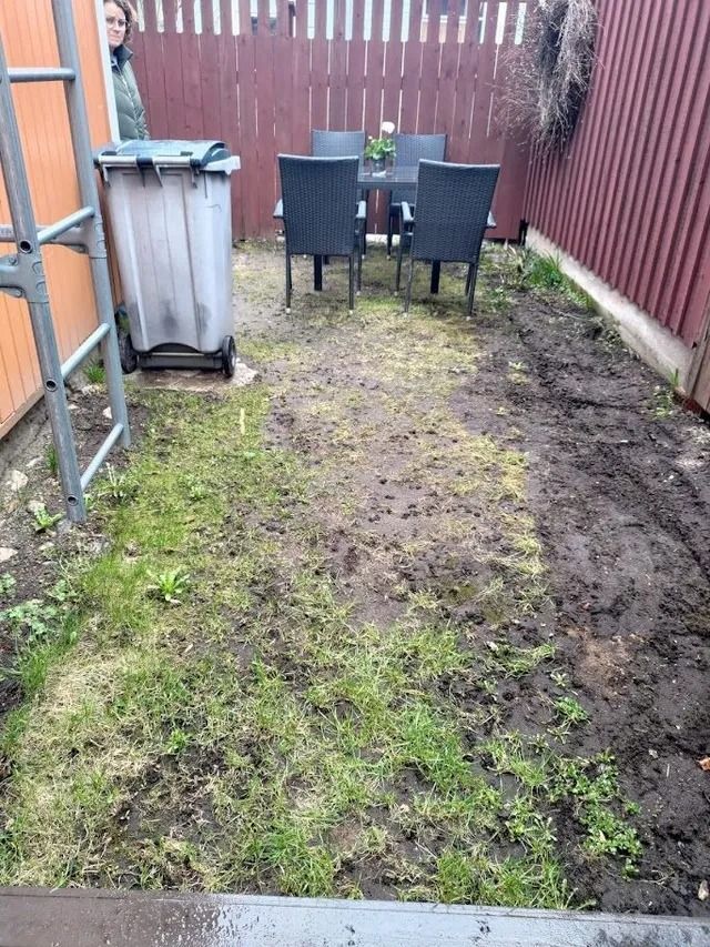 Kapea mutainen takapiha, jossa pieni terassipöytä ja tuolit punaista aitaa vasten