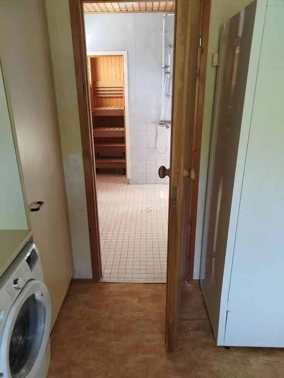 Kapea käytävä, jonka vasemmalla puolella on pesukone, oikealla valkoinen kaappi ja edessä laatoitettu oviaukko.
