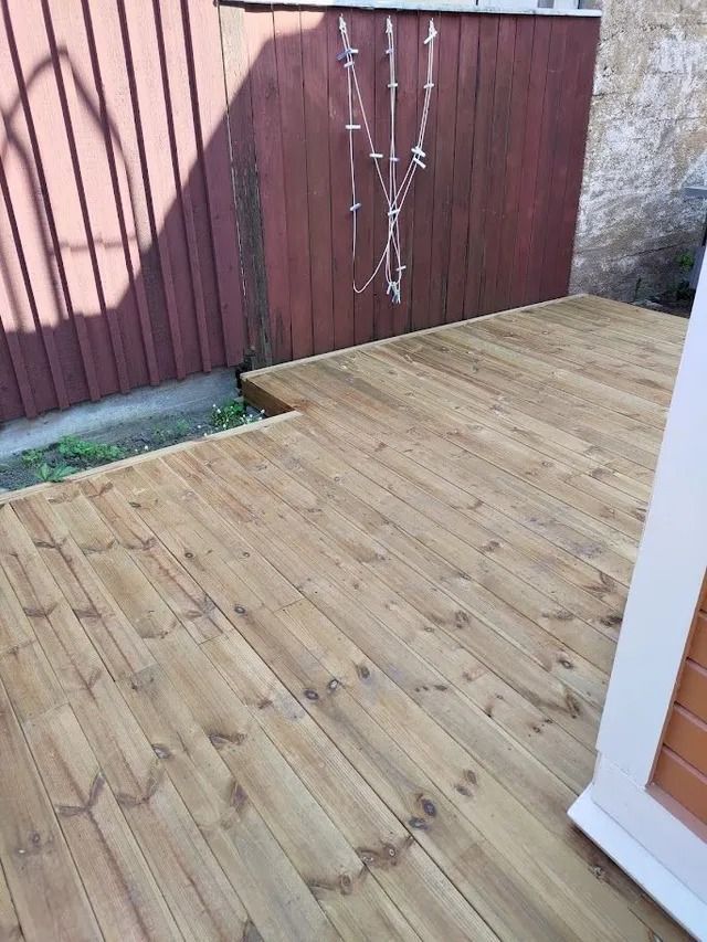 Puinen patiokansi punaisen aidan ja kivimuurin vieressä, pieni puu nurkassa.