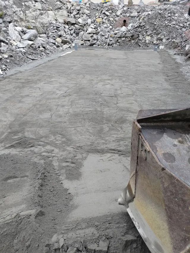 Tuore harmaa betonilaatta rakennustyömaalla, taustalla rauniokasat ja etualalla koneiden reuna