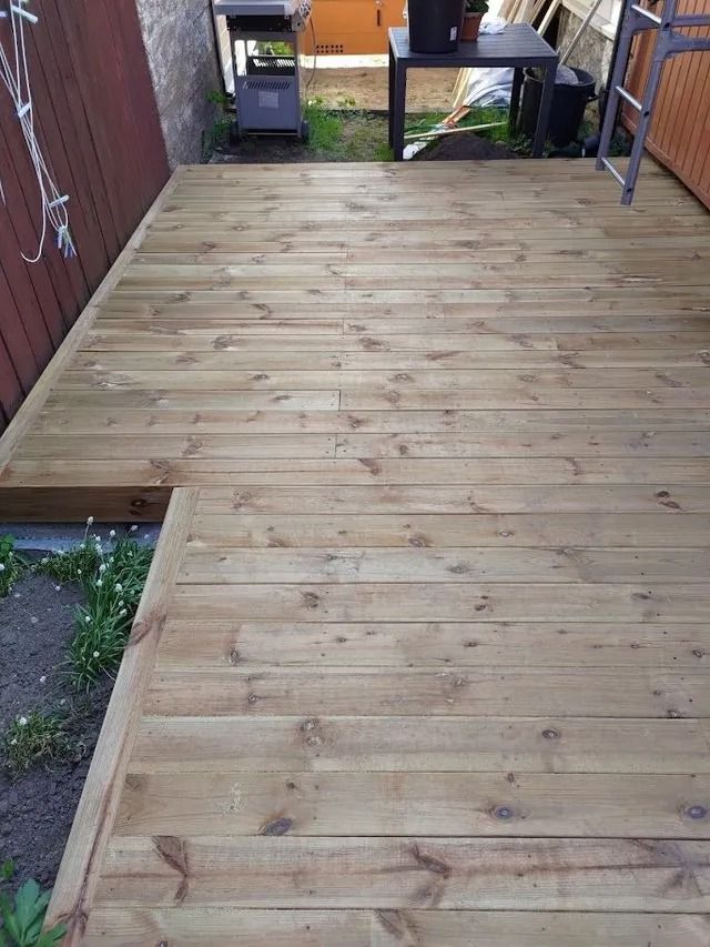 Tuore puinen terassikäytävä tiiliseinien välissä, joka johtaa pienelle patioalueelle.