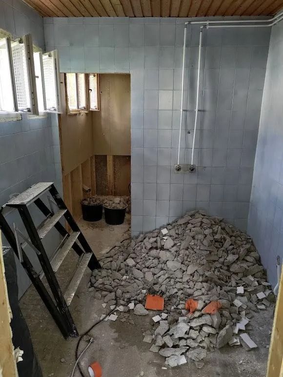 Remontissa oleva kylpyhuone, jossa lattialla on kivimurskaa, tikkaat ja seinät laatoitetut.
