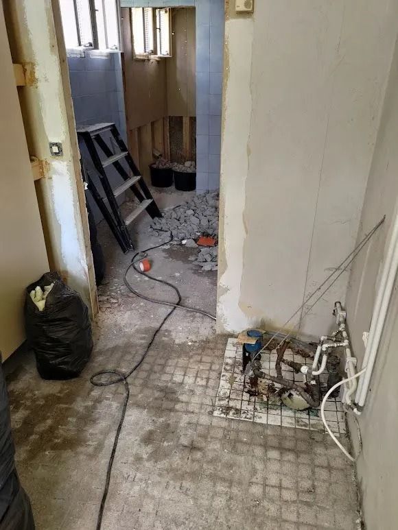 Kapea käytävä rakenteilla, jossa on roskia, näkyvillä johtoja ja seinää vasten nojaavat tikkaat.
