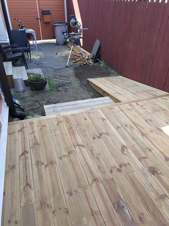 Puinen terassi rakenteilla kapean sorapihan ja punaisen aidan vieressä, jossa on työkaluja ja istutusastioita.