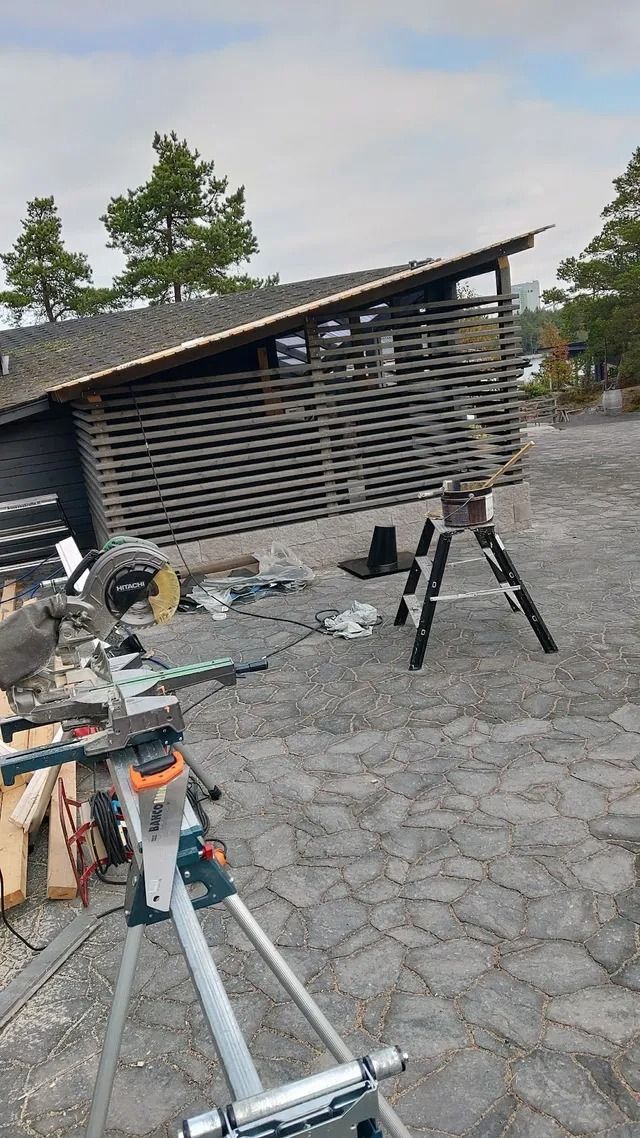 Ulkona oleva työmaa, jossa on jalustalle asennettuja laitteita, puinen vaja ja mukulakivikato pilvisen taivaan alla