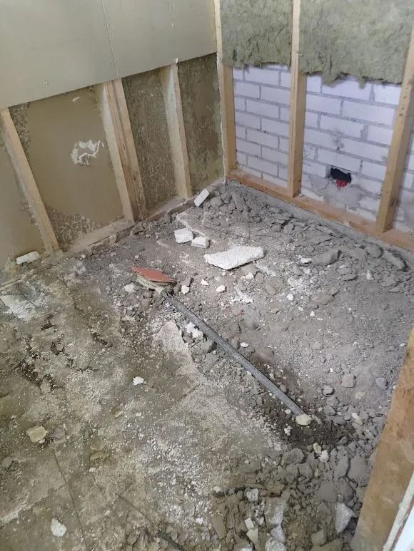 Purettu huone, jossa näkyvät seinätuet, soran peittämä lattia ja osittain laatoitettu seinä.