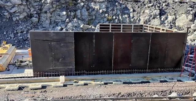 Suuri musta teollinen metallirakennelma rautatien vieressä kivisellä rakennustyömaalla