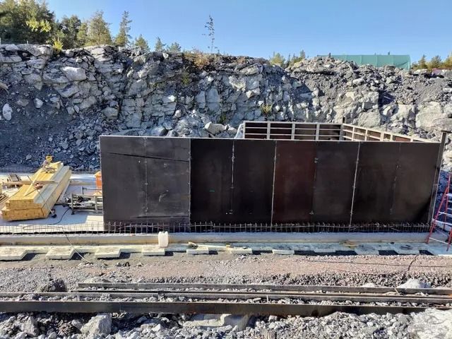 Musta metallinen aita rautatien vieressä kivisellä rakennustyömaalla, jossa on kaivinkoneita ja tikkaat
