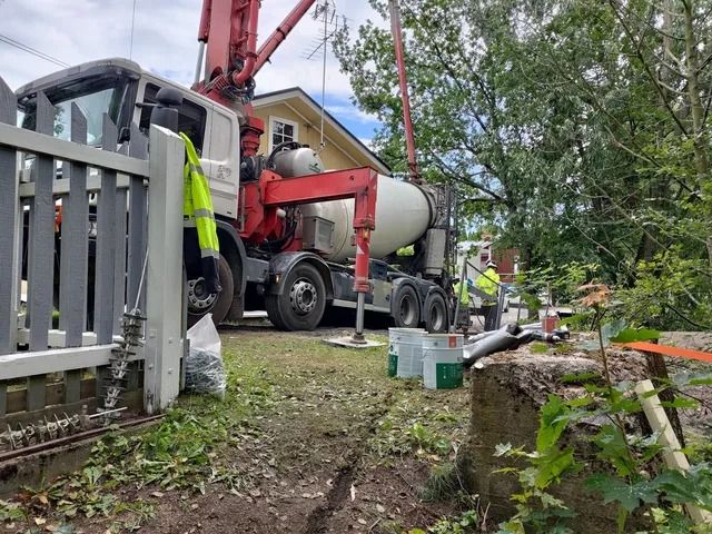 Betonimyllyauto ja pumppu rakennustyömaalla talon ja aidan vieressä.