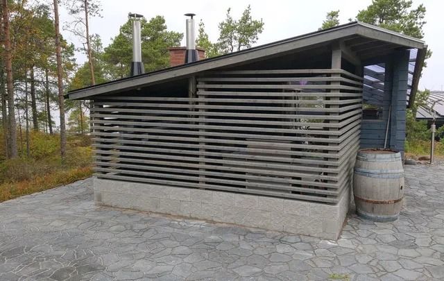 Moderni puinen mökki, jossa on vaakasuoria säleitä ja kivinen patio metsäisellä alueella
