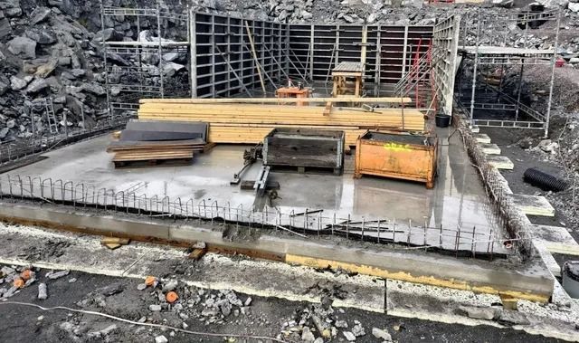 Rakennusperustus, jossa on raudoitusta, betonilaattaa ja pinottuja materiaaleja kiviaineksen peittämällä tontilla