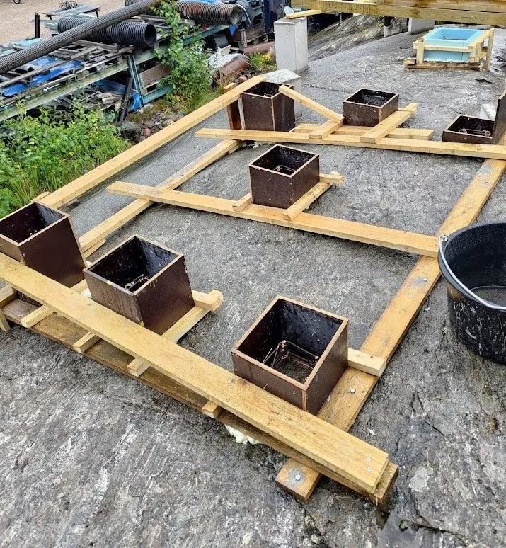 Puinen runko, jossa neljä neliönmuotoista metallista istutusruukkua, betonipinnalla ulkona.