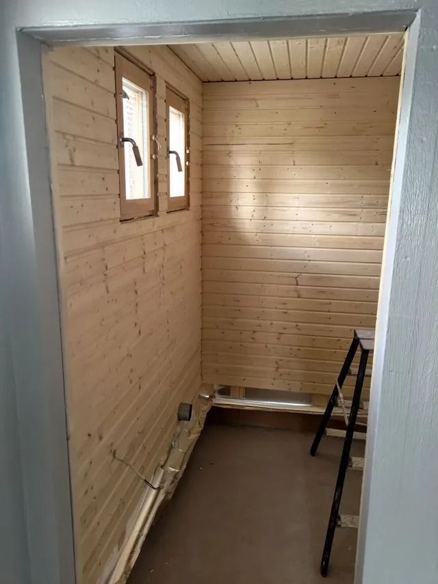 Tyhjä kapea puuhuone remontissa, ikkunat vasemmalla ja tikkaat oikealla.