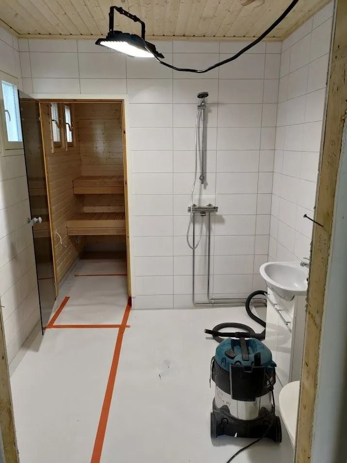 Pieni remontoitava kylpyhuone, jossa suihku, wc, pölynimuri ja keskeneräinen puuovi