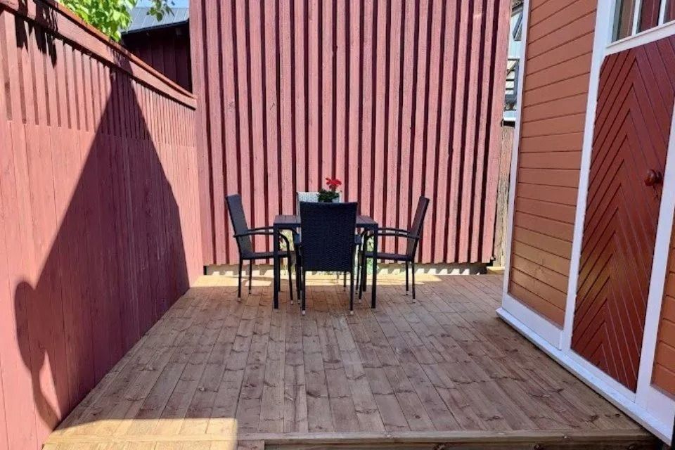 Tyhjä puinen patio, jossa musta pöytä ja tuolit punaisten aitojen ja seinien välissä.
