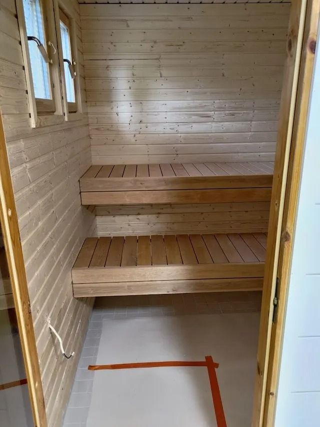 Pieni puinen sauna, jossa on kaksi laudetta ja harmaa lattia.