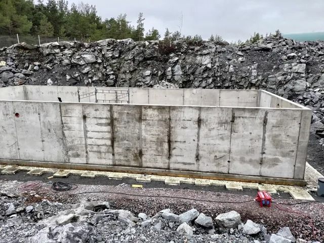 Betoninen tukimuuri kallioisen maan ja kivipenkereen vieressä pilvisen taivaan alla