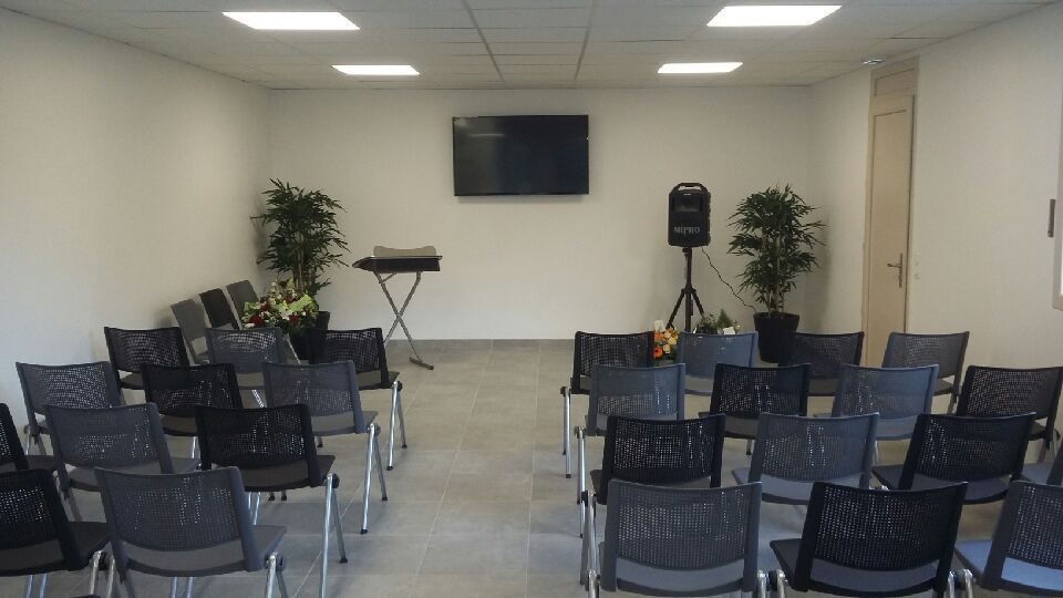 Salle de conférence vide avec des rangées de chaises face à un écran, un podium et un orateur.